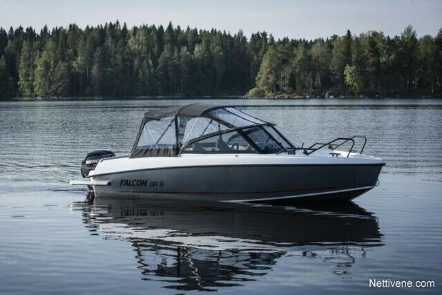 A Falcon BR 6 boat is cruising on a calm lake surrounded by lush green trees, reflecting on the water's surface.